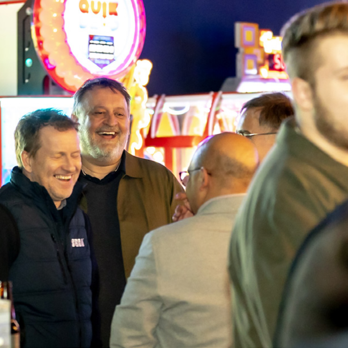 Group of friends laughing over drinks with neon lighting.